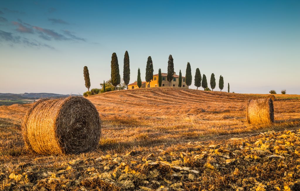 Beautiful Tuscany landscape with traditional farm house and hay bales in golden evening light, Val d'Orcia, Italy